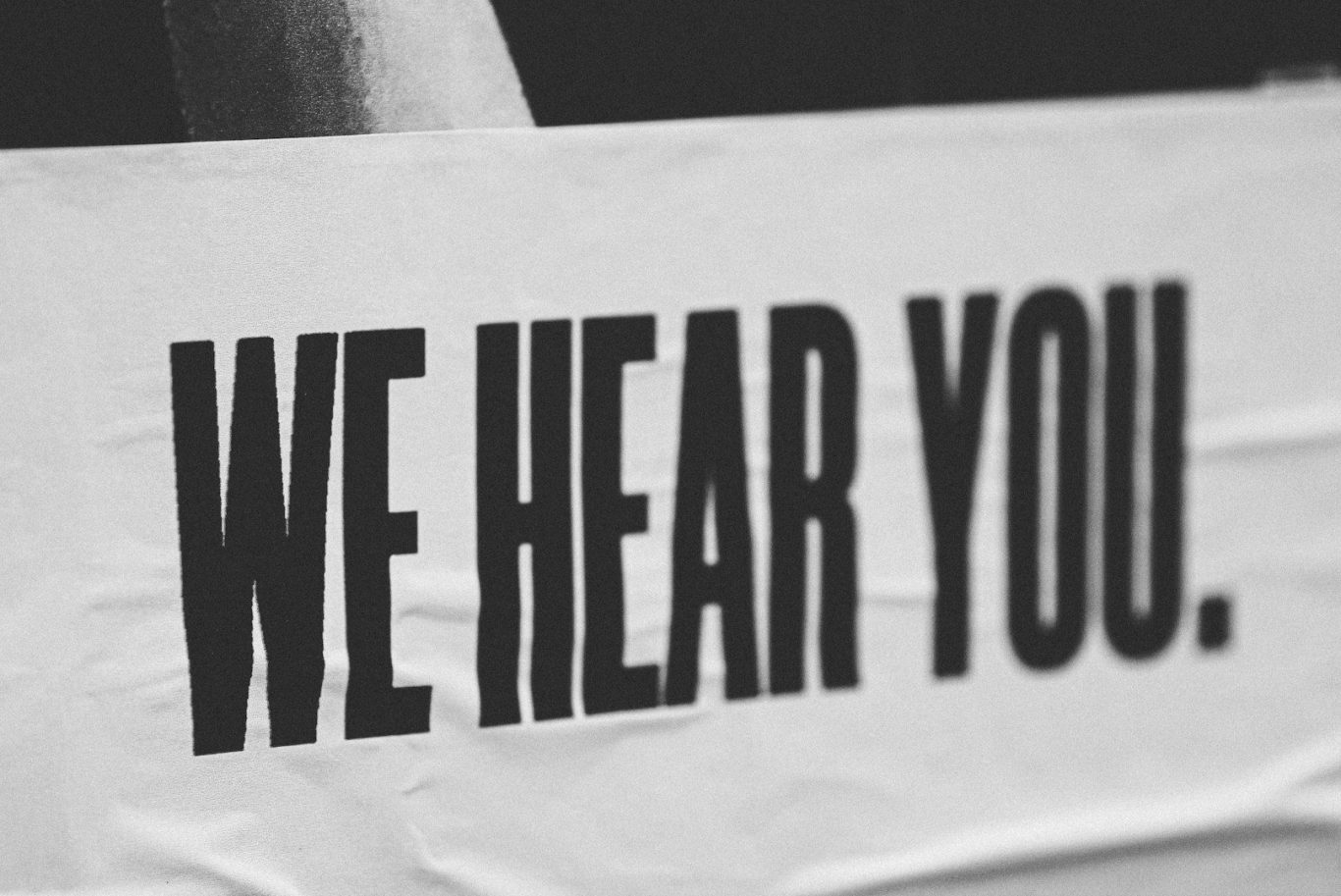 Schriftzug „WE HEAR YOU“ in großer, fetter Schrift auf einem Banner.